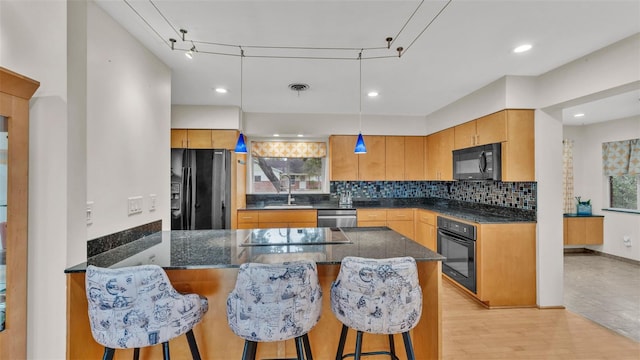 kitchen featuring sink, hanging light fixtures, light wood-type flooring, a kitchen breakfast bar, and black appliances