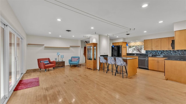 kitchen with hanging light fixtures, light wood-type flooring, a kitchen breakfast bar, decorative backsplash, and black appliances