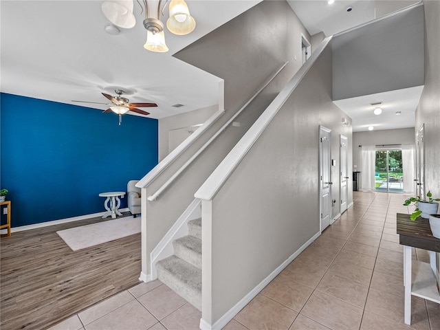 staircase with light hardwood / wood-style flooring and ceiling fan with notable chandelier