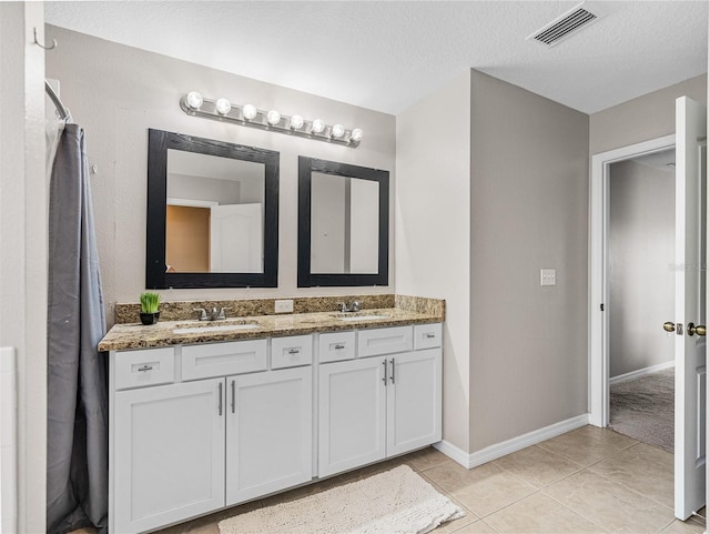 bathroom with double vanity, tile patterned flooring, and a textured ceiling