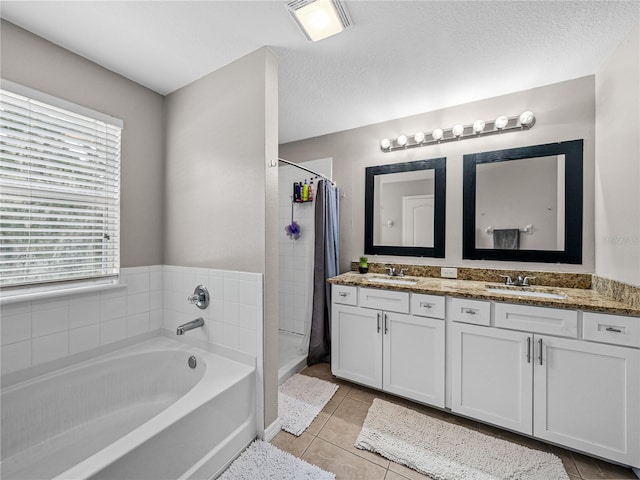 bathroom with tile patterned flooring, a tub, a textured ceiling, and dual bowl vanity