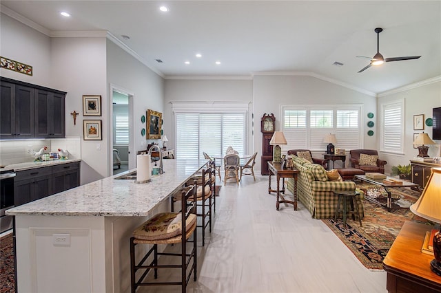 kitchen featuring light stone countertops, vaulted ceiling, plenty of natural light, and a center island with sink