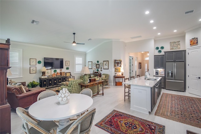 kitchen with sink, crown molding, stainless steel refrigerator with ice dispenser, light stone counters, and a center island with sink