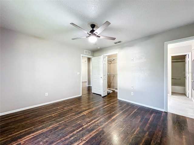 unfurnished bedroom featuring a spacious closet, a closet, a textured ceiling, ceiling fan, and wood-type flooring