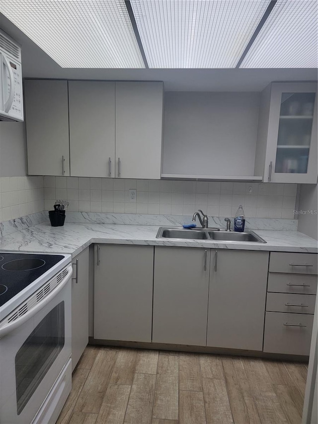 kitchen featuring white appliances, gray cabinetry, sink, backsplash, and light wood-type flooring