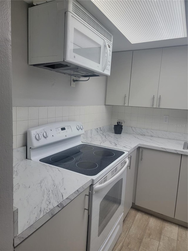 kitchen with gray cabinets, light hardwood / wood-style floors, light stone countertops, and white appliances