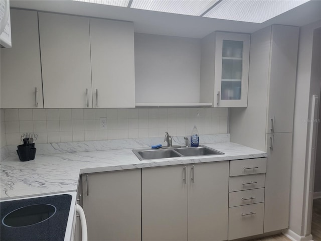 kitchen featuring backsplash, light stone counters, hardwood / wood-style floors, stove, and sink