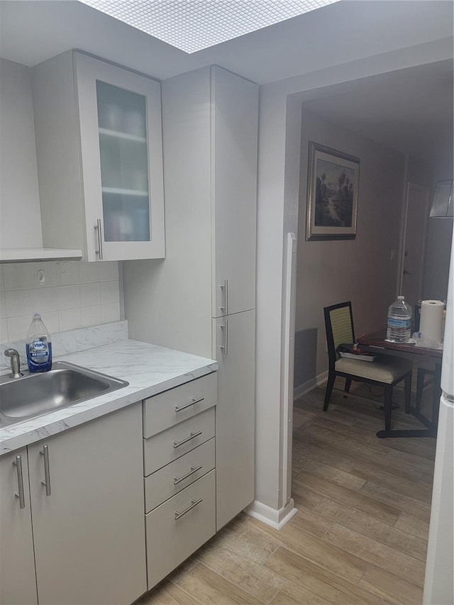 kitchen featuring decorative backsplash, light hardwood / wood-style flooring, light stone counters, and sink