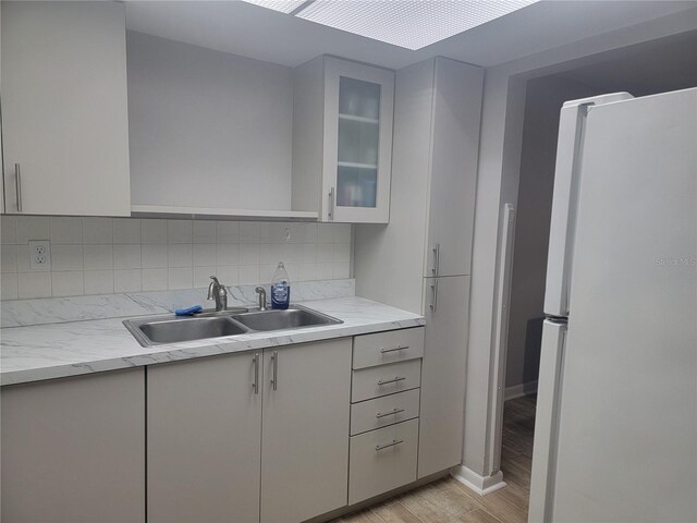 kitchen with tasteful backsplash, light hardwood / wood-style floors, sink, and white fridge