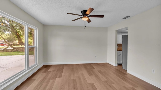 spare room featuring ceiling fan, light wood-type flooring, and a textured ceiling