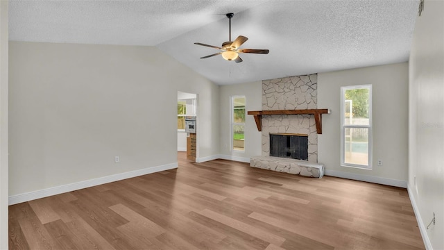 unfurnished living room with ceiling fan, light wood-type flooring, a textured ceiling, and a stone fireplace