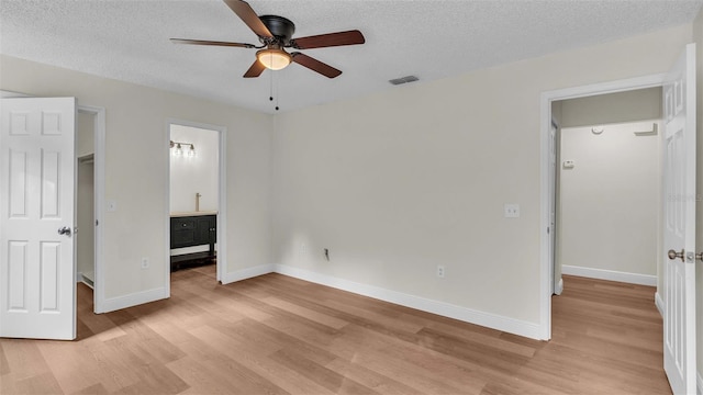 unfurnished bedroom featuring a textured ceiling, ceiling fan, a spacious closet, light hardwood / wood-style floors, and ensuite bath