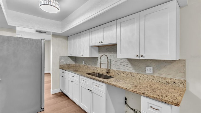 kitchen featuring white cabinets, sink, light hardwood / wood-style flooring, and stainless steel fridge