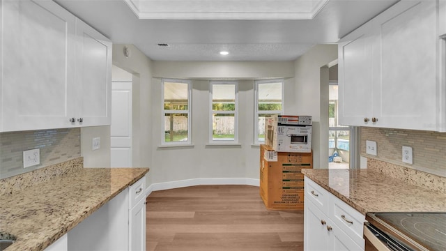 kitchen with white cabinets, backsplash, light hardwood / wood-style flooring, and light stone counters