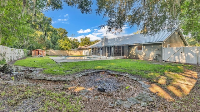 rear view of property featuring a sunroom, a patio area, a yard, and a storage shed