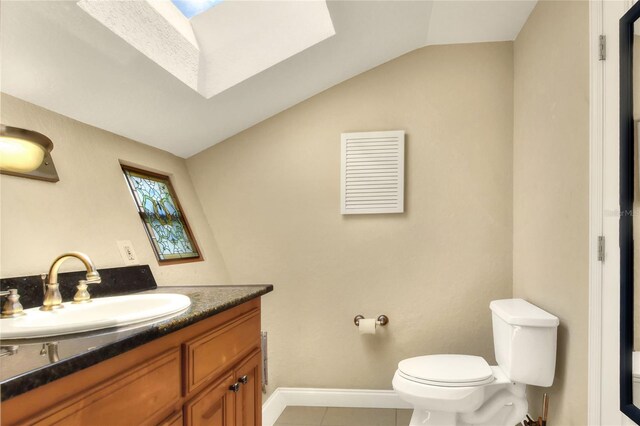 bathroom featuring vanity, toilet, vaulted ceiling with skylight, and tile patterned flooring