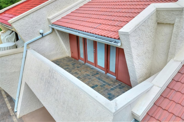 exterior details with gutters, a downspout, a tile roof, and stucco siding