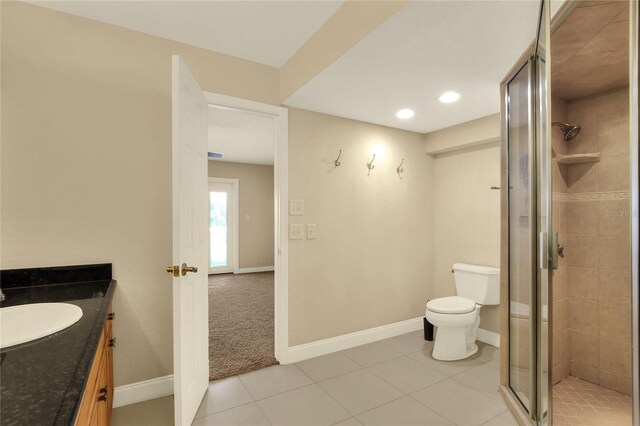 bathroom with a shower with door, vanity, tile patterned flooring, and toilet