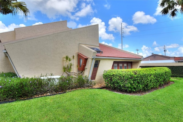 view of property exterior featuring a lawn, a tiled roof, and stucco siding