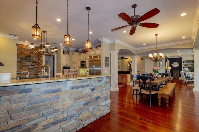 kitchen featuring light stone countertops, dark wood-type flooring, cream cabinets, decorative light fixtures, and appliances with stainless steel finishes