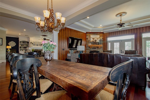 dining room with a stone fireplace, dark wood-type flooring, and ceiling fan with notable chandelier