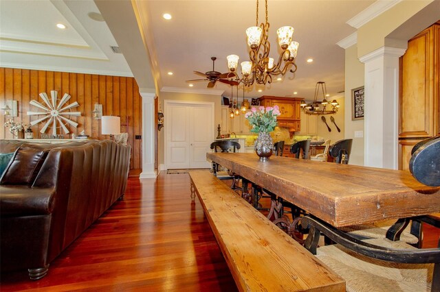 dining room featuring decorative columns, crown molding, dark wood-type flooring, and ceiling fan with notable chandelier