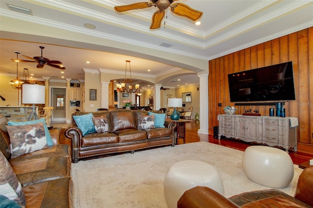 living room with dark wood-type flooring, decorative columns, crown molding, wood walls, and a tray ceiling