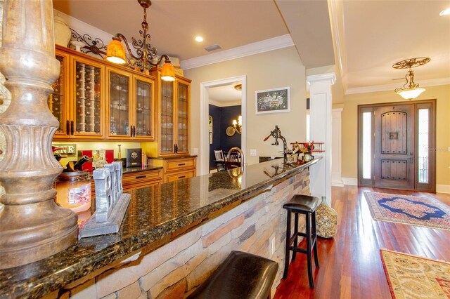 bar with pendant lighting, dark stone counters, dark hardwood / wood-style floors, and ornamental molding