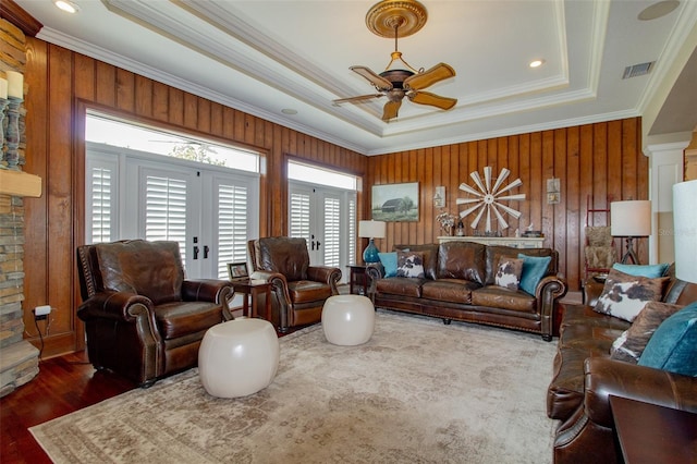 living room featuring french doors, ornamental molding, a tray ceiling, dark hardwood / wood-style floors, and wood walls