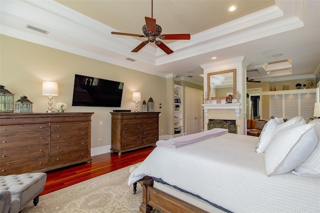 bedroom featuring a raised ceiling, ensuite bath, crown molding, and dark wood-type flooring