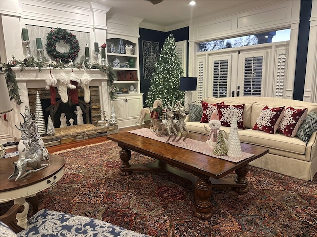 living room with a stone fireplace, crown molding, and hardwood / wood-style flooring