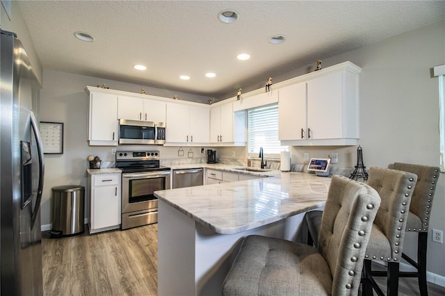 kitchen with appliances with stainless steel finishes, sink, a breakfast bar area, white cabinets, and kitchen peninsula