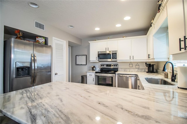 kitchen featuring white cabinetry, sink, kitchen peninsula, stainless steel appliances, and light stone countertops