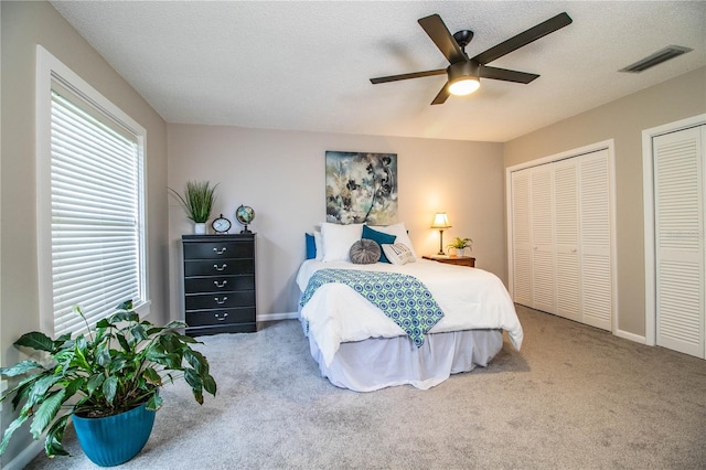 carpeted bedroom with ceiling fan, two closets, and a textured ceiling