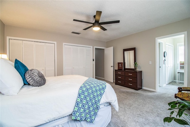 carpeted bedroom with multiple closets, ceiling fan, and a textured ceiling