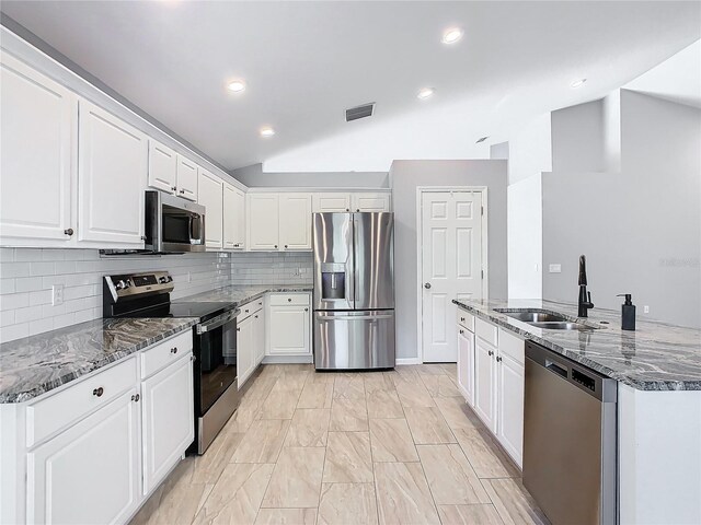 kitchen with dark stone counters, appliances with stainless steel finishes, lofted ceiling, tasteful backsplash, and white cabinets