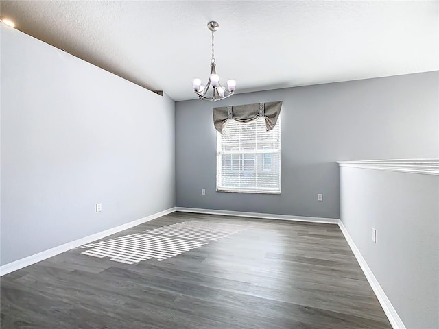 spare room featuring an inviting chandelier, a textured ceiling, baseboards, and dark wood-type flooring