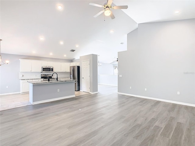 kitchen featuring ceiling fan with notable chandelier, stainless steel appliances, white cabinetry, open floor plan, and a center island with sink