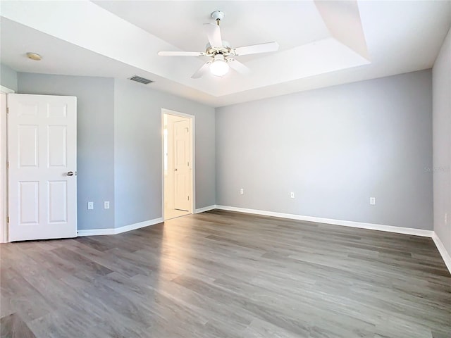 unfurnished room with ceiling fan, dark wood-type flooring, a raised ceiling, and baseboards