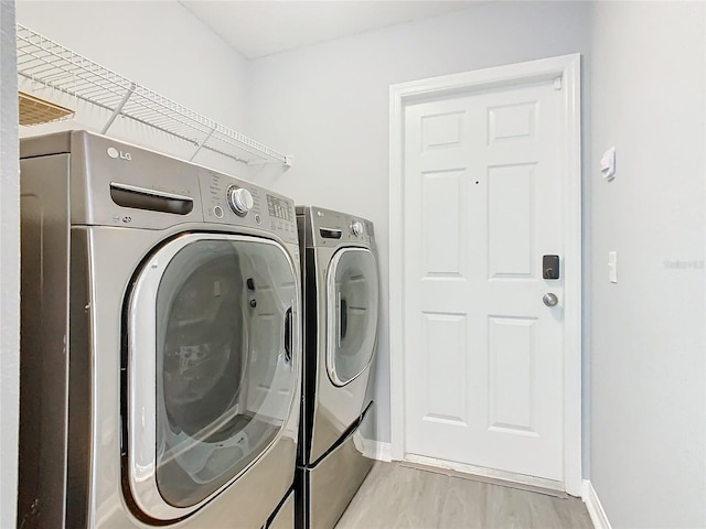 clothes washing area featuring light wood-style floors, laundry area, baseboards, and separate washer and dryer