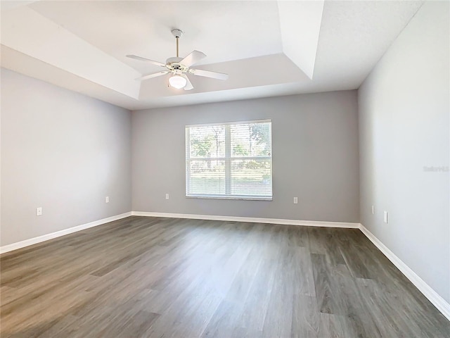 unfurnished room with dark wood-type flooring, a raised ceiling, baseboards, and a ceiling fan