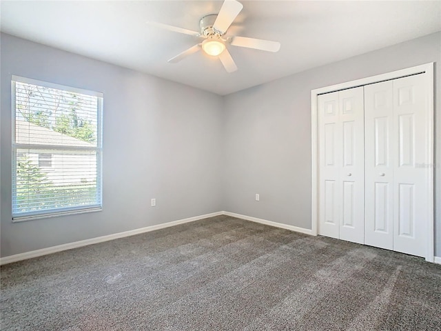 unfurnished bedroom with ceiling fan, a closet, dark carpet, and baseboards