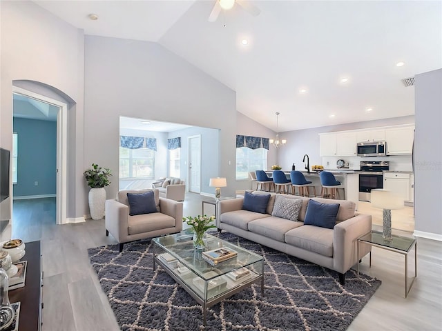 living room with ceiling fan with notable chandelier, high vaulted ceiling, light wood-style flooring, visible vents, and baseboards