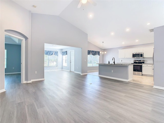 unfurnished living room with light wood-style flooring, visible vents, high vaulted ceiling, ceiling fan with notable chandelier, and a sink