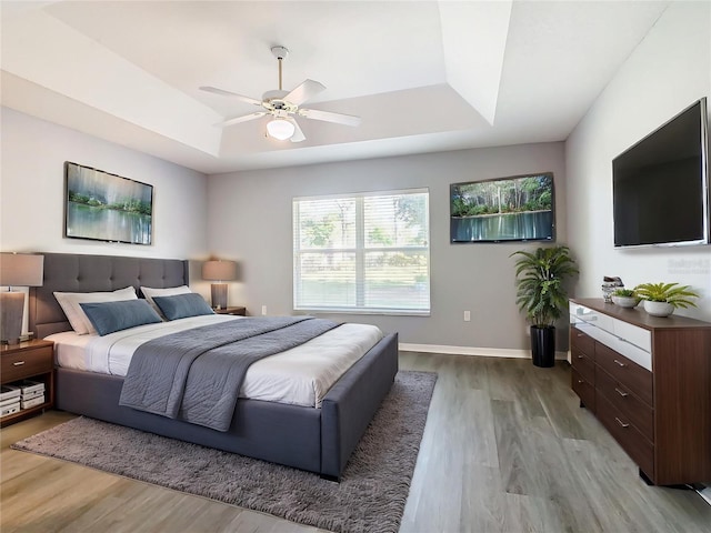 bedroom with baseboards, wood finished floors, a ceiling fan, and a raised ceiling