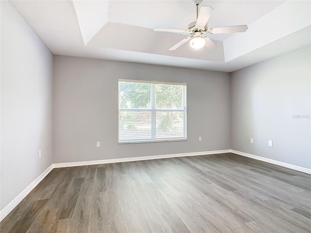 empty room featuring a tray ceiling, baseboards, a ceiling fan, and wood finished floors