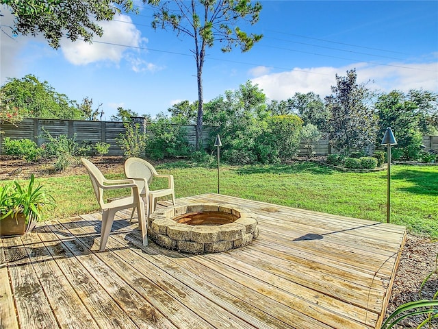 wooden deck featuring an outdoor fire pit, a fenced backyard, and a lawn
