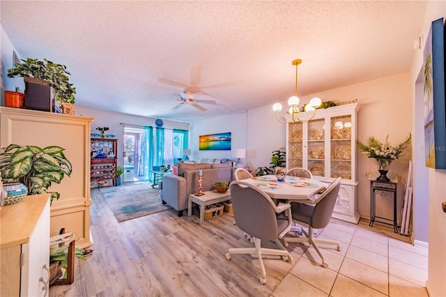 dining space with light hardwood / wood-style floors, ceiling fan with notable chandelier, and a textured ceiling