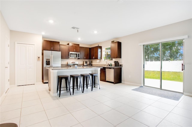 kitchen with a breakfast bar area, light tile patterned flooring, stainless steel appliances, and a kitchen island