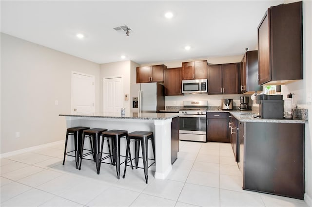 kitchen featuring a kitchen breakfast bar, light tile patterned flooring, appliances with stainless steel finishes, light stone counters, and a kitchen island